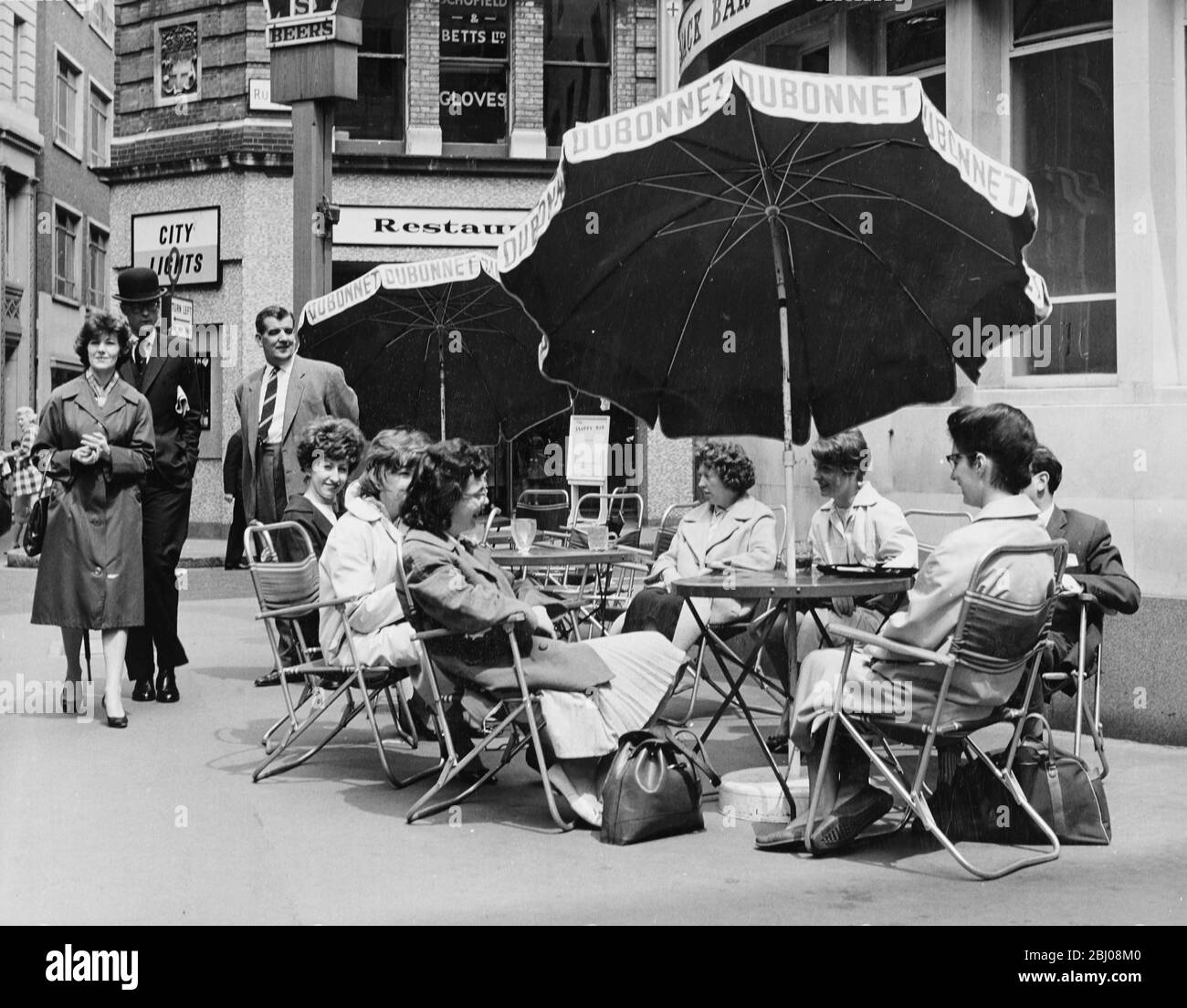 Le ragazze dell'ufficio prendono il loro pranzo pausa al fresco in un tavolo e un ombrello stile continentale sul marciapiede fuori di una casa pubblica a Milk Street, Londra. - 12 giugno 1962 Foto Stock