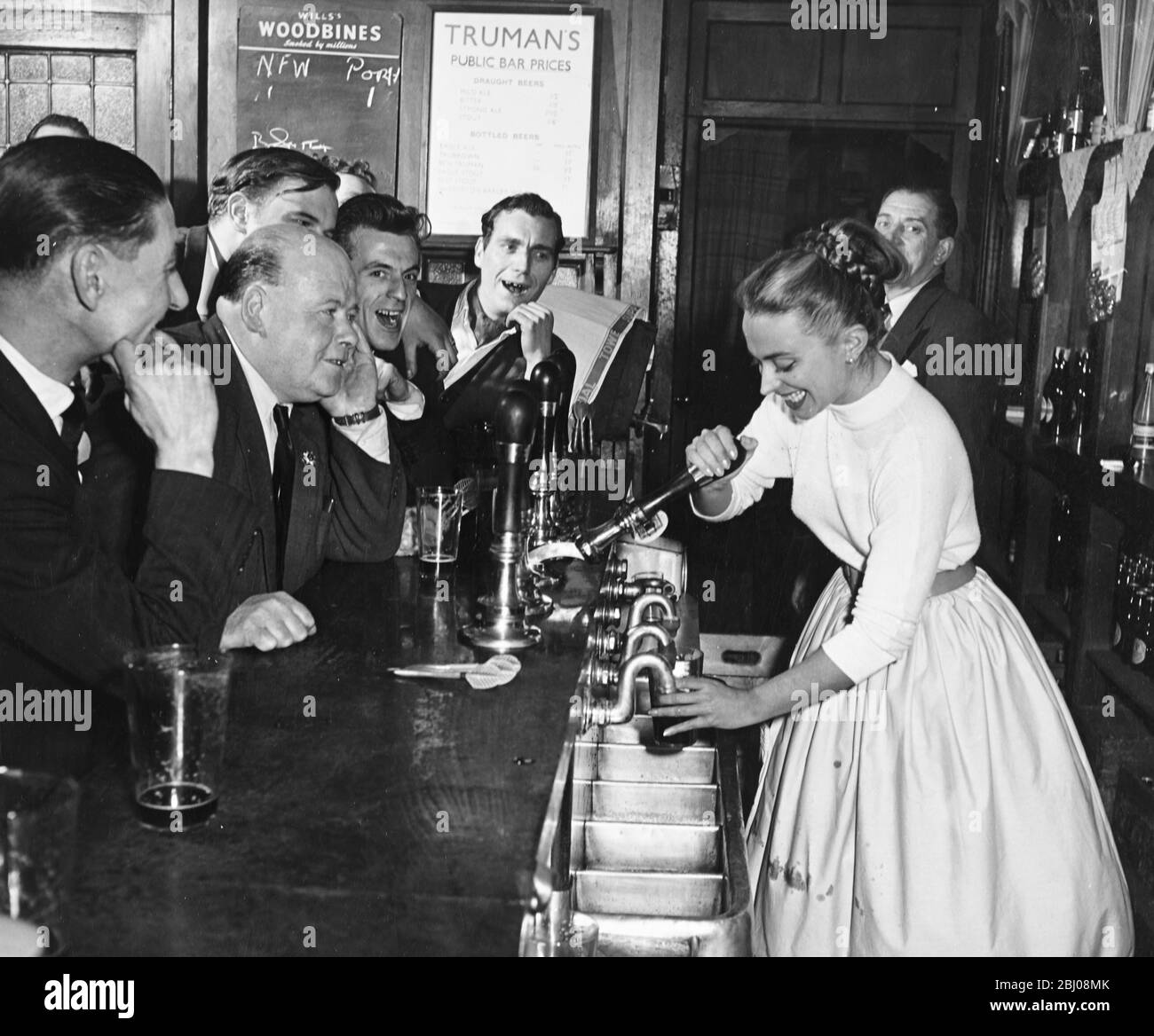 Una donna barbaraid tira una pinta di birra per i clienti maschi in un pub londinese , Inghilterra. - anni '50 Foto Stock