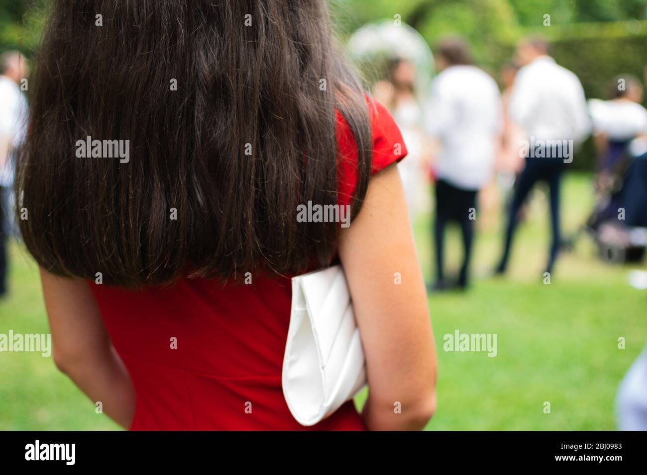 Retro di donna che indossa abiti rossi e borsa bianca per la festa all'aperto Foto Stock