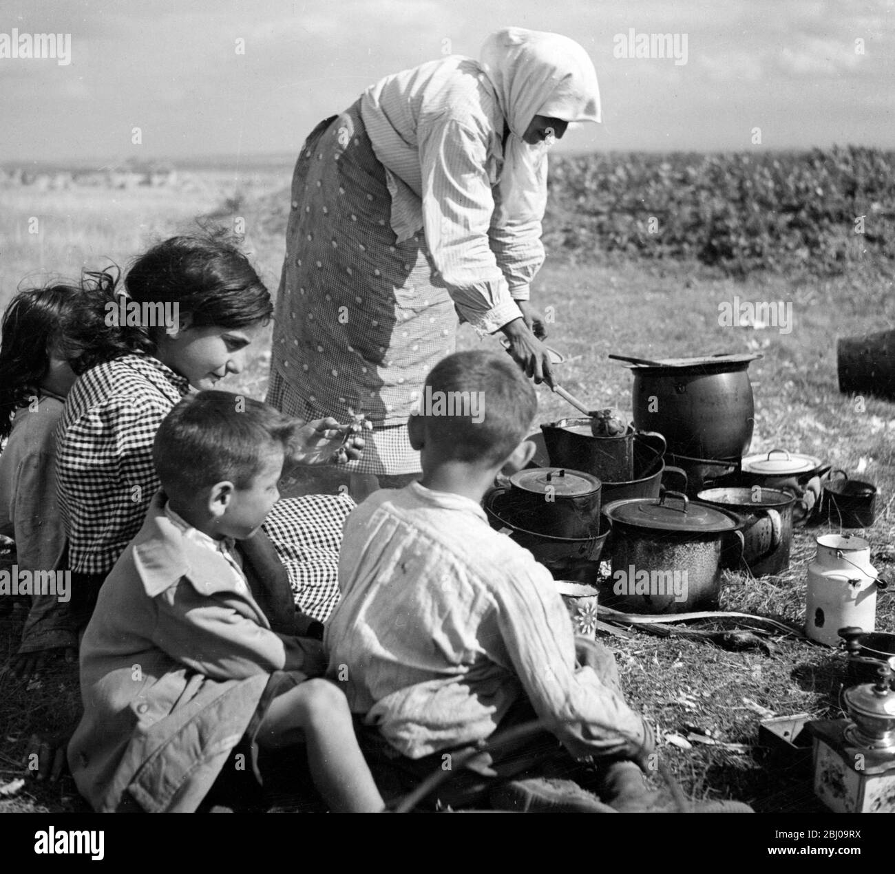 Donna serve cibo da pentole di cottura ai bambini in un campo. non datato Foto Stock