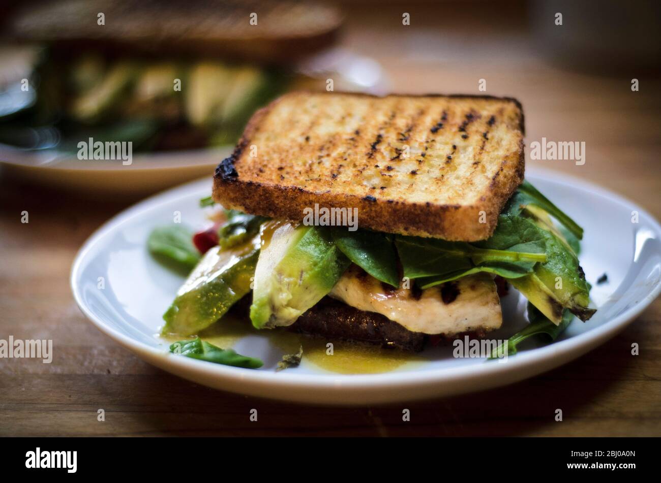 Pane senza glutine alla griglia utilizzato per preparare un panino di filetto di pollo grigliato, fette di avocado, spinaci, pepe rosso con vinaigrette. Foto Stock