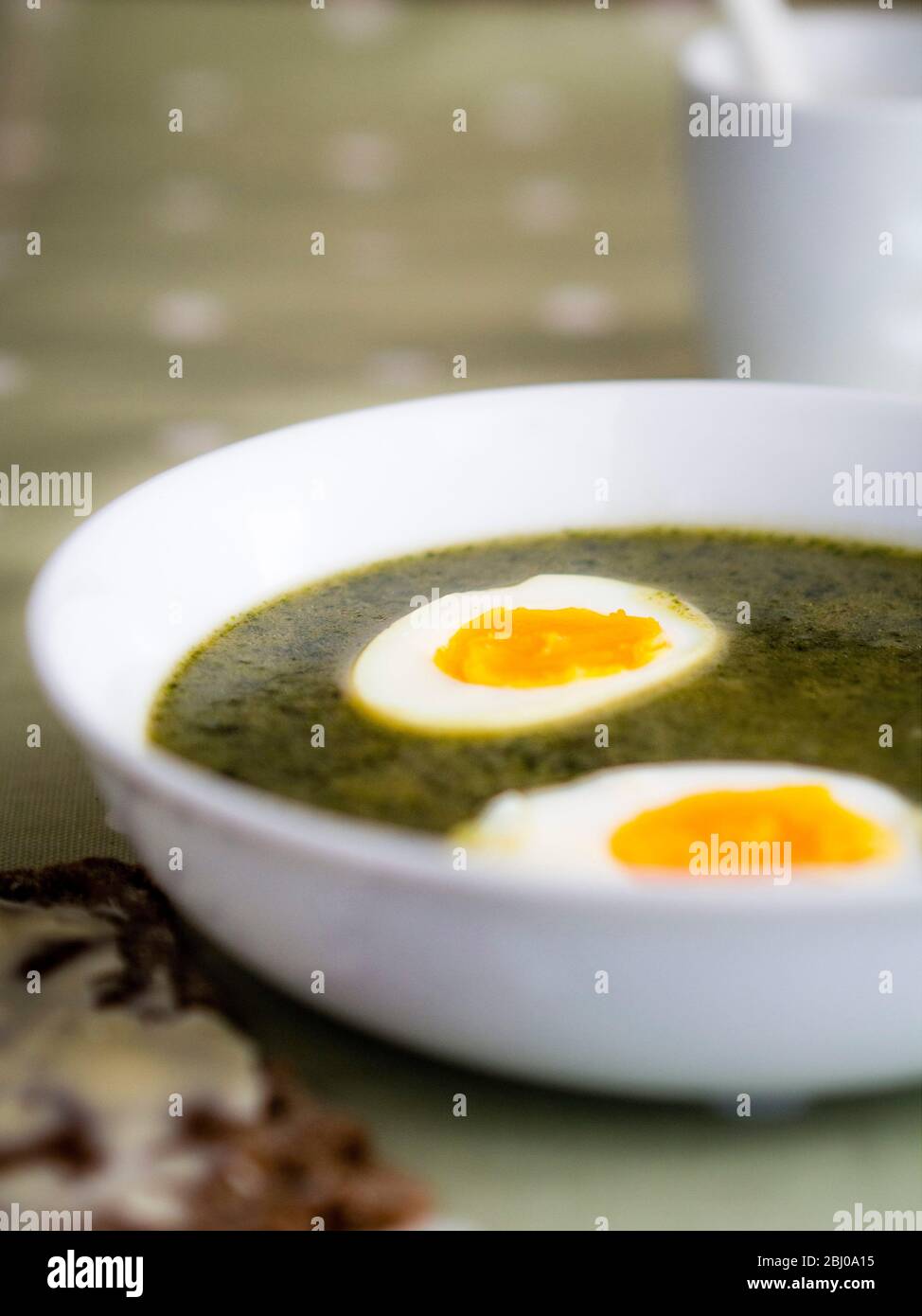 Ciotola bianca di zuppa di ortica svedese su panno a righe con cucchiaio d'argento su panno di verdure macchiato con knÌÄå ckebrÌÄå¦d svedese (pane croccante di segale e bu Foto Stock