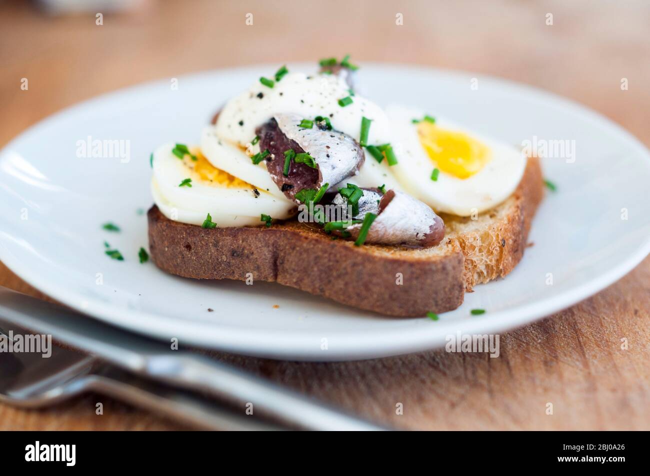 Un classico panino svedese a vista aperta con uova sode a fette, condite con ansjovis svedese in scatola (spratti sottaceto) cosparso di erba cipollina tritata. Foto Stock
