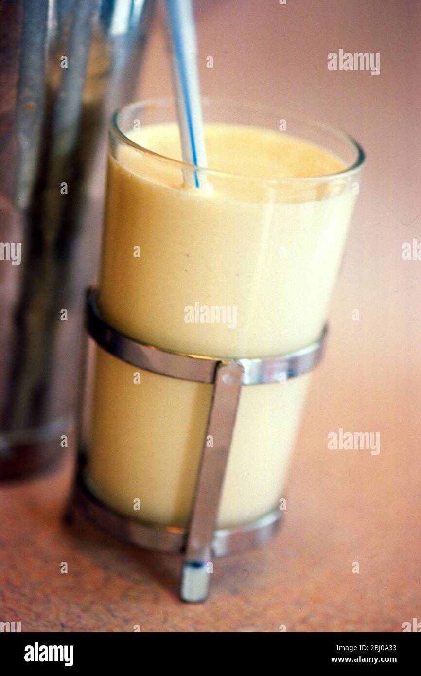 Shake di latte di banana in vetro di gabbia con paglia striata sul banco di pranzo - Foto Stock