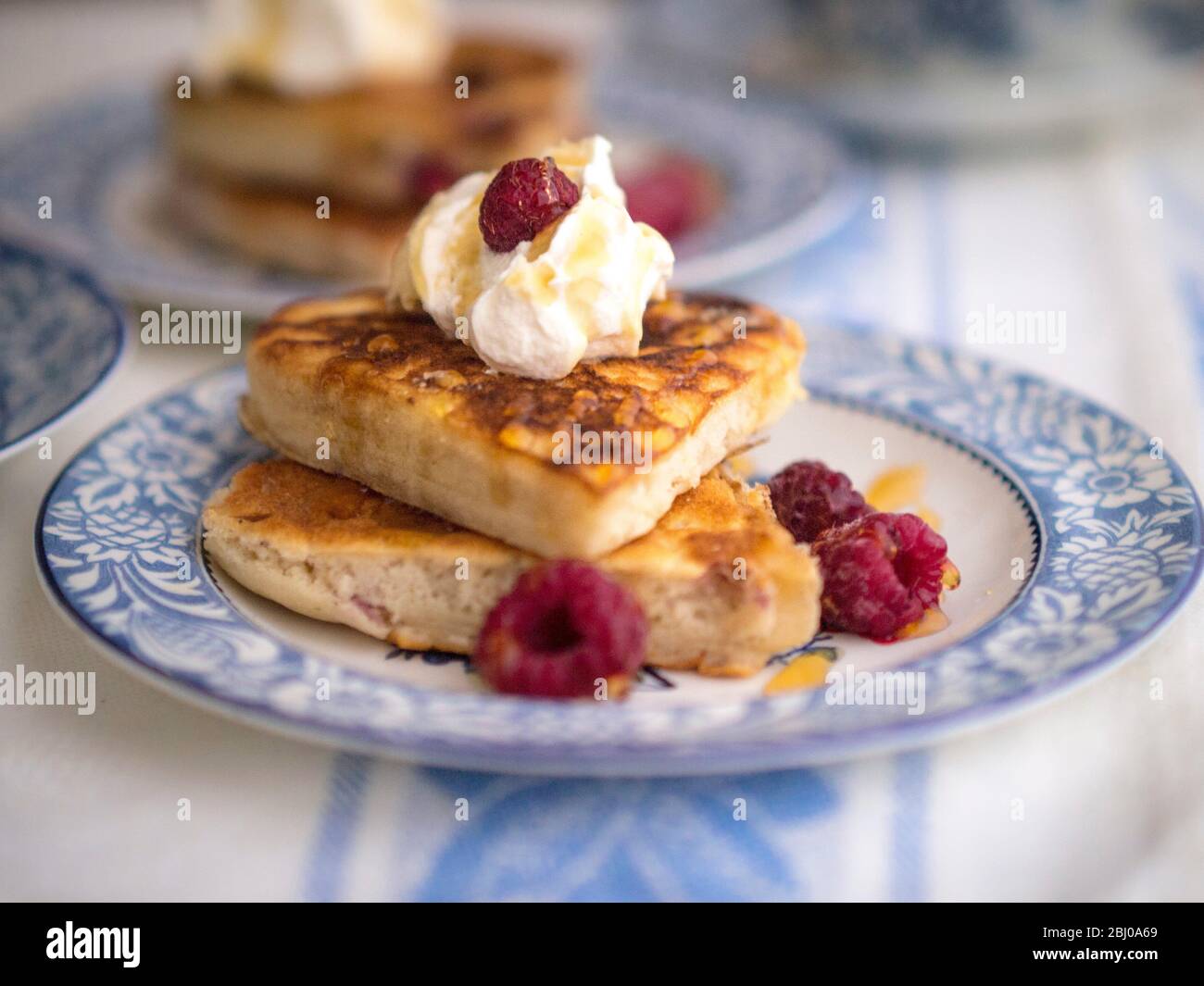 Pancake a base di frittelle a cuore serviti con panna montata, lamponi e un filo di miele. Foto Stock