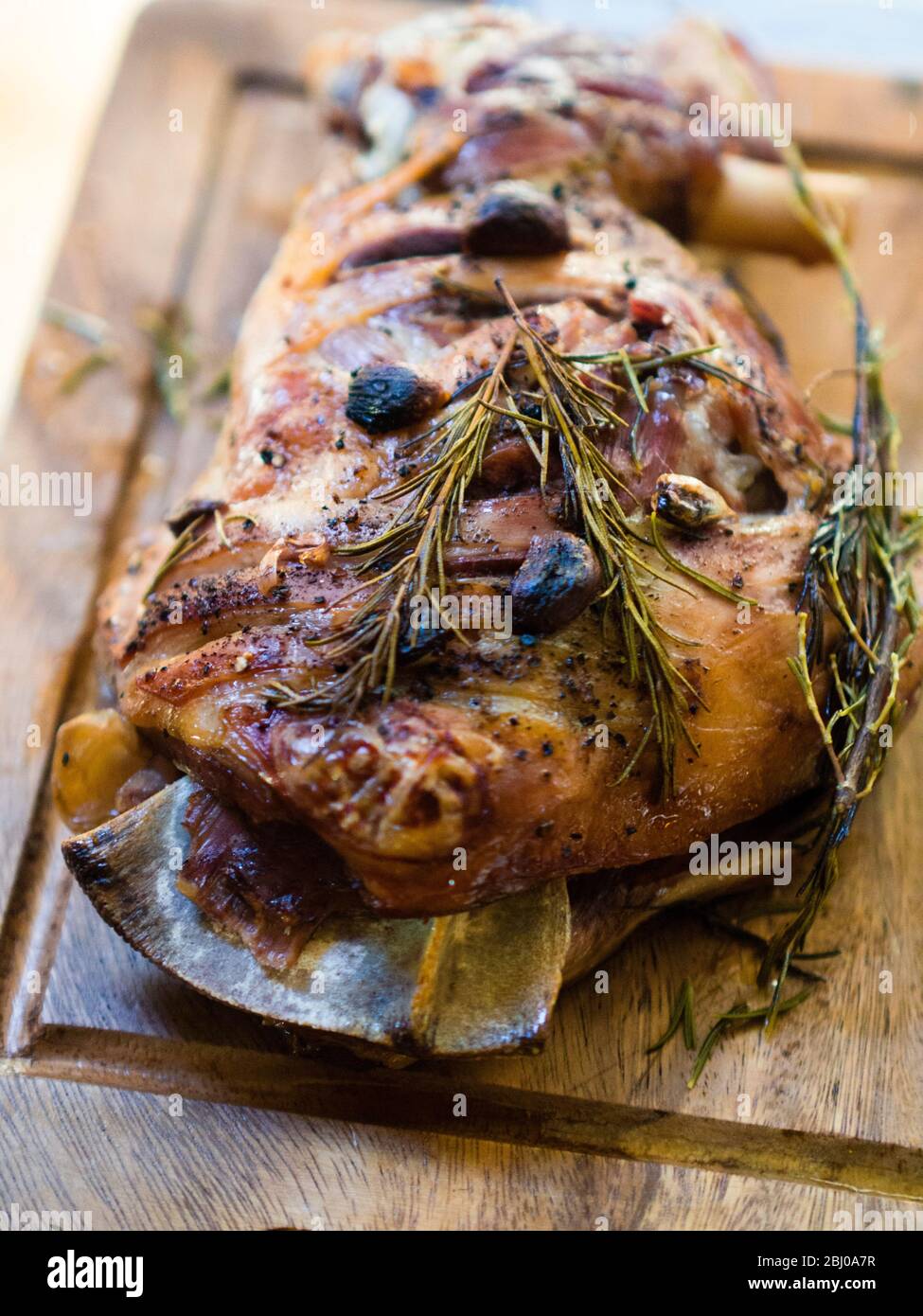 Spalla di agnello a tostatura lenta con aglio e rosmarino, su tavola di legno Foto Stock