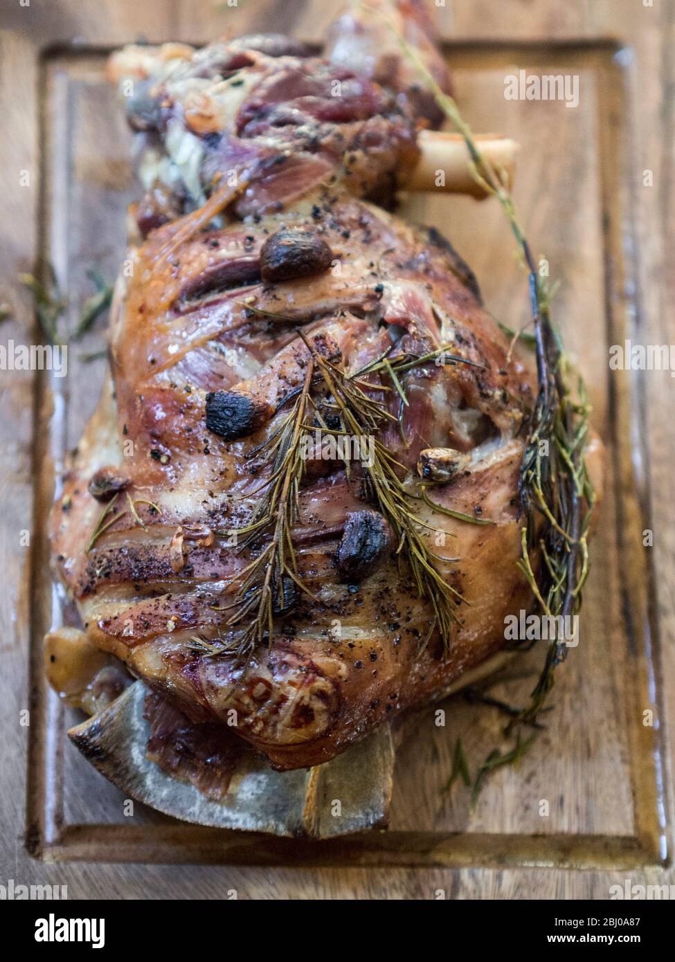 Spalla di agnello a tostatura lenta con aglio e rosmarino, su tavola di legno Foto Stock