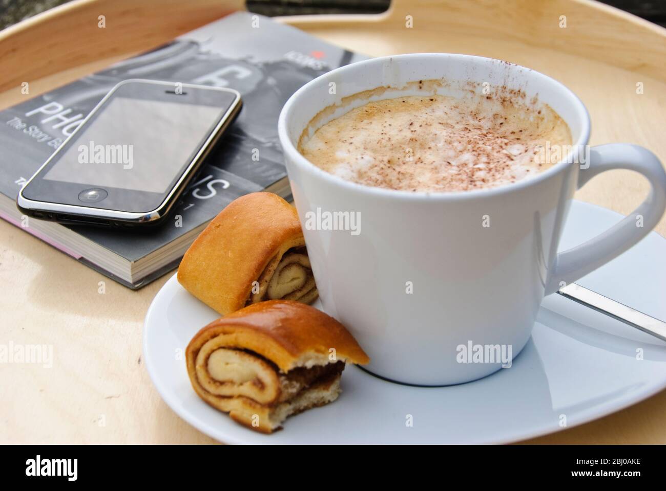 Grande cip bianco di cappuccino caffè con iphone telefono cellulare e libro cartaceo - Foto Stock