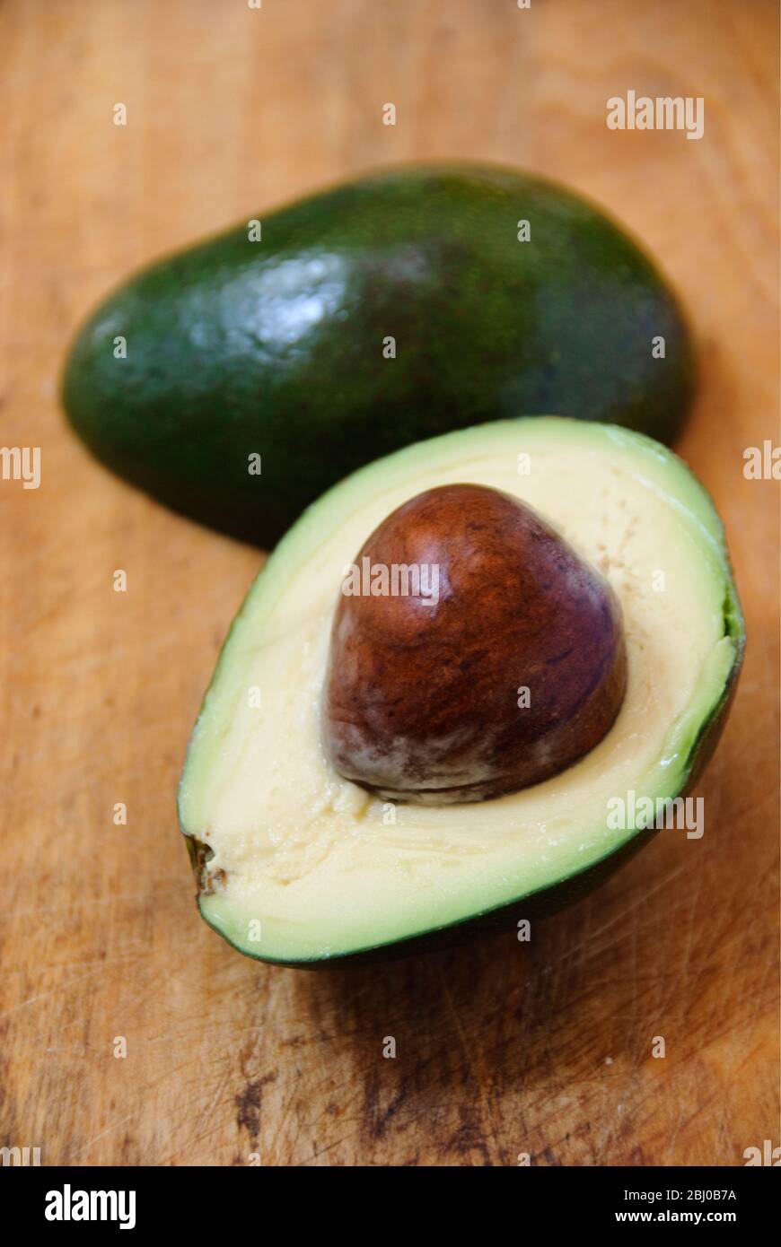 Pera di avocado fresca intera e tagliata su sfondo di legno - Foto Stock