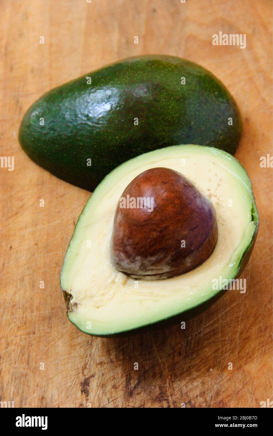 Pera di avocado fresca intera e tagliata su sfondo di legno - Foto Stock