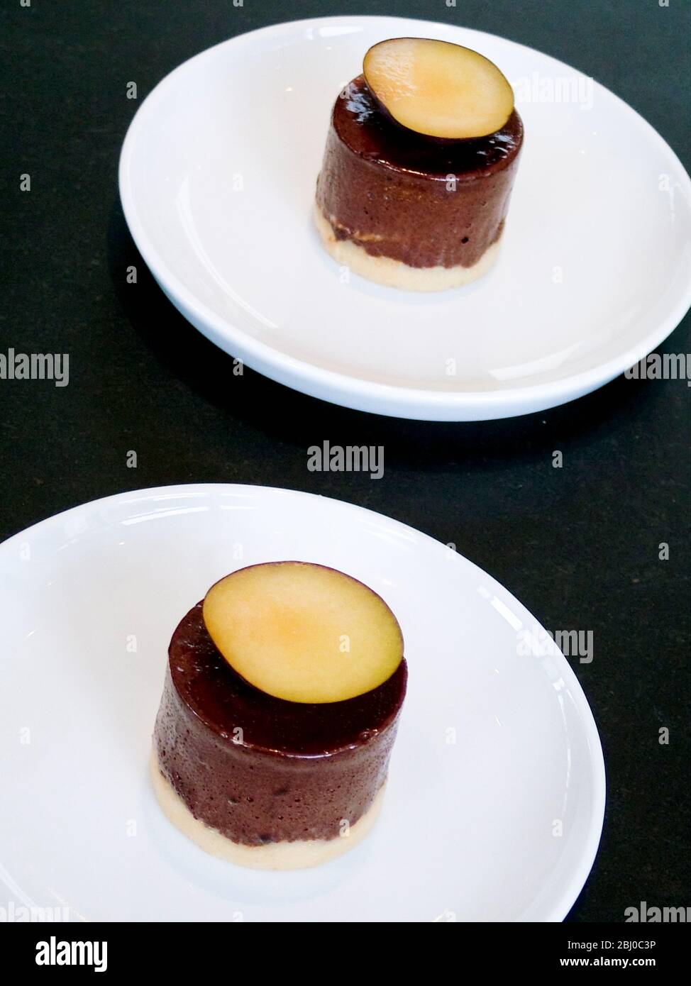 Mousse al cioccolato con fetta di prugna su piatto bianco - Foto Stock