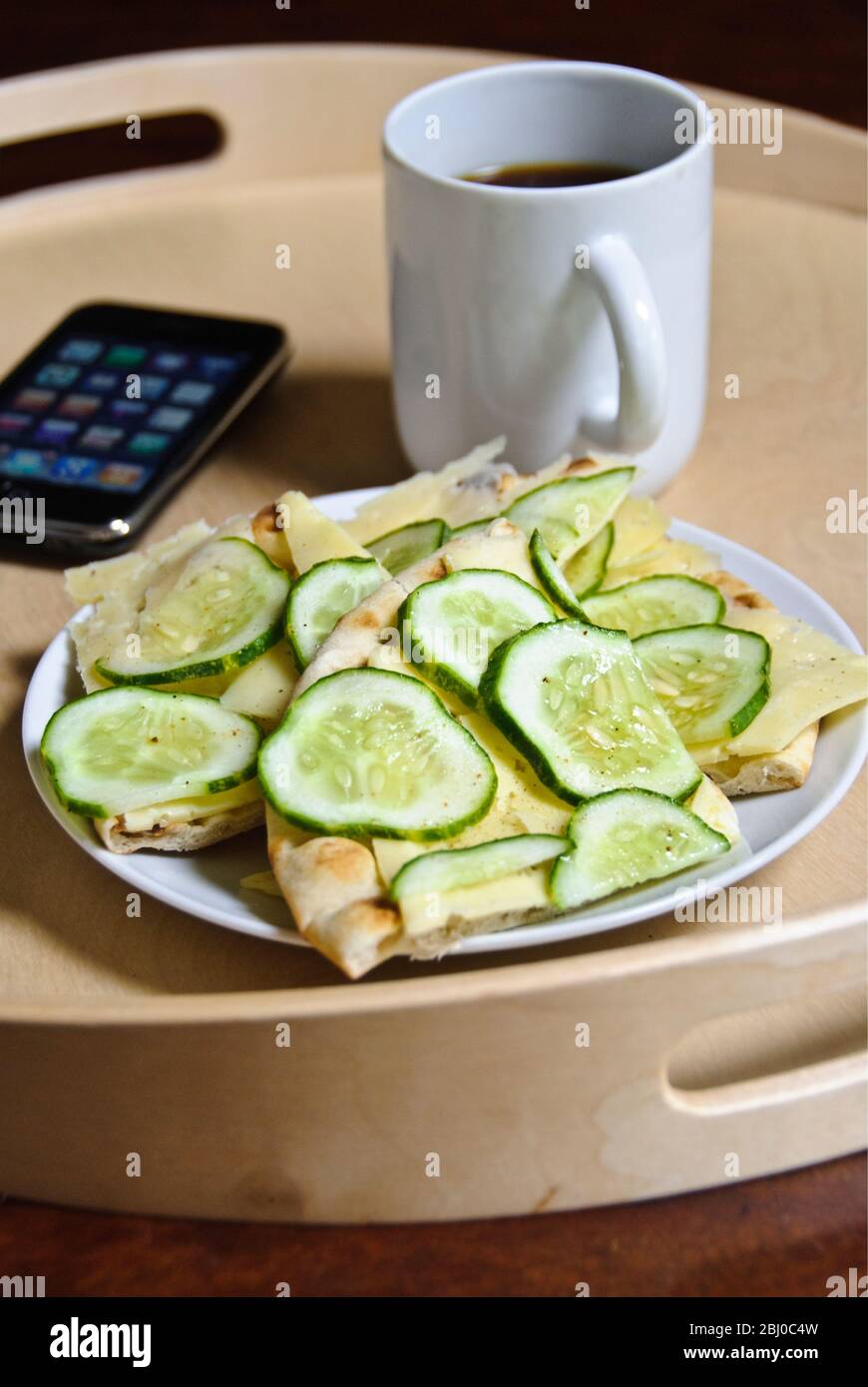 Spuntino di pane piatto scandinavo, con fette di formaggio svedese e cetrioli sottili, cosparso di sale alle erbe, con una tazza di caffè nero e iphone o Foto Stock