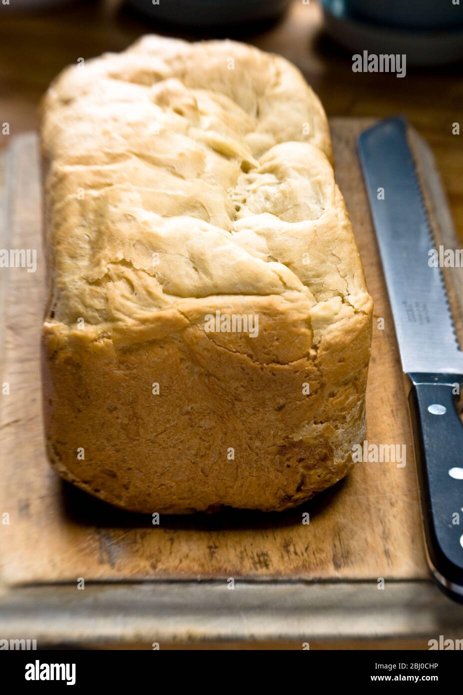 Pane bianco crostoso con farina biologica in paniera elettrica su paniera di legno vecchio con coltello seghettato - Foto Stock