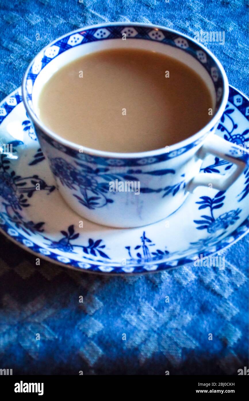 Tazza bianca e blu antica e piattino di tè indiano con latte, su tovaglia blu - Foto Stock
