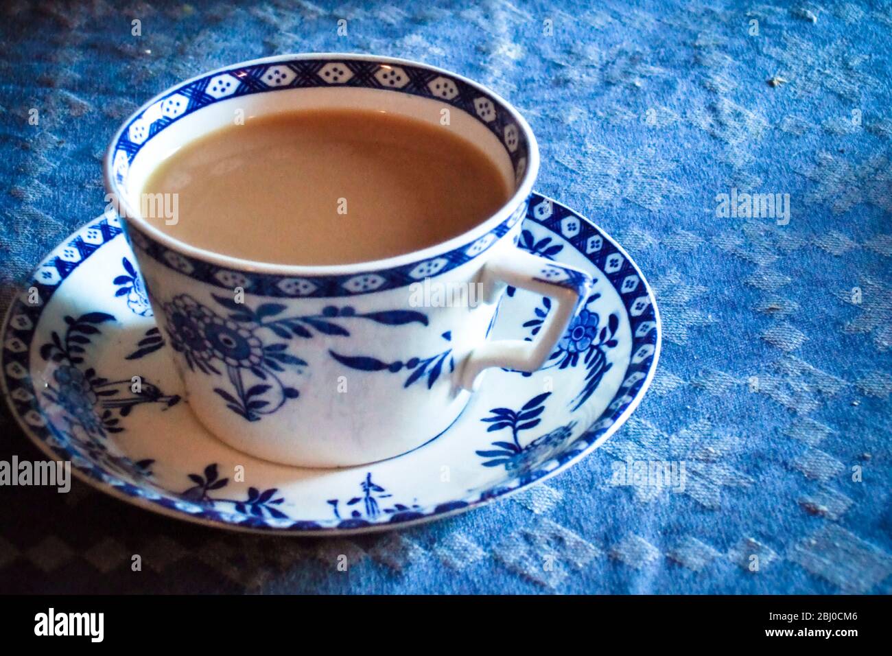 Tazza bianca e blu antica e piattino di tè indiano con latte, su tovaglia blu - Foto Stock
