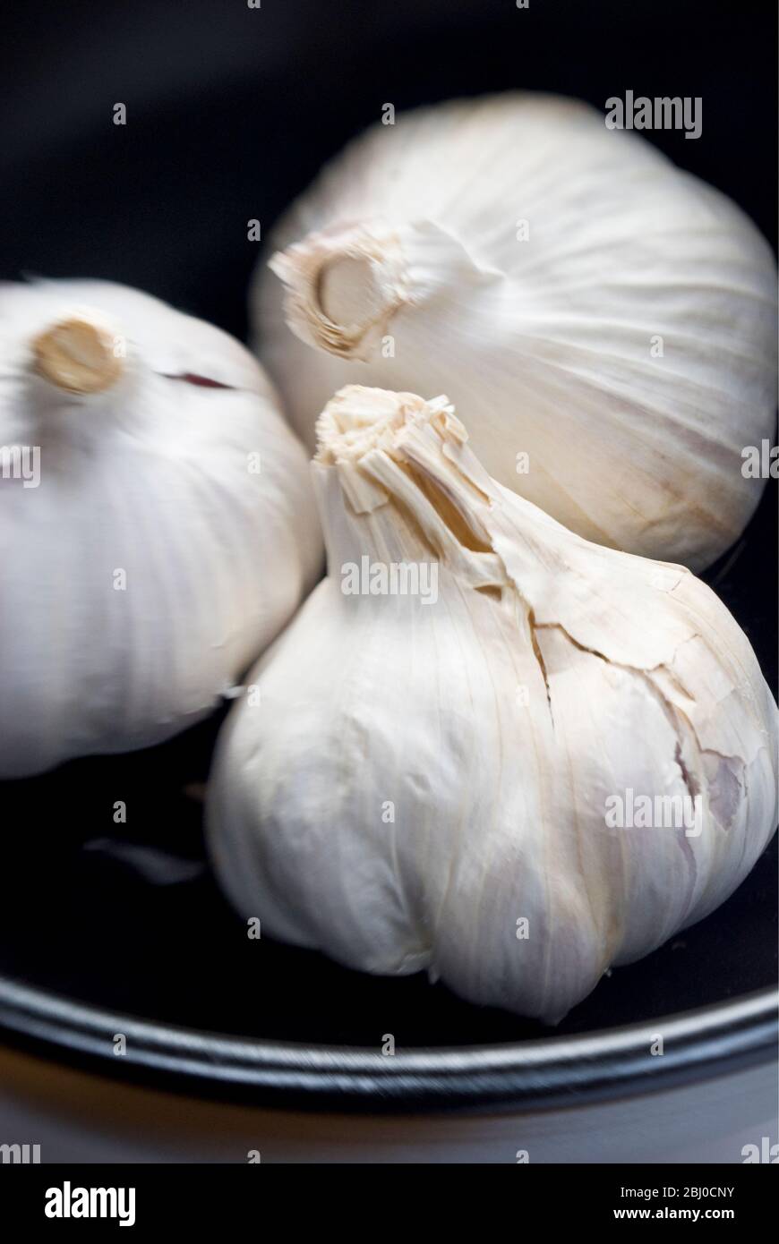 Tre bulbi interi di aglio in ciotola nera - Foto Stock