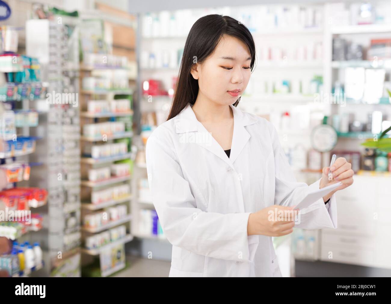 Donna cinese cercando medicina con notebook vicino scaffali in farmacia Foto Stock