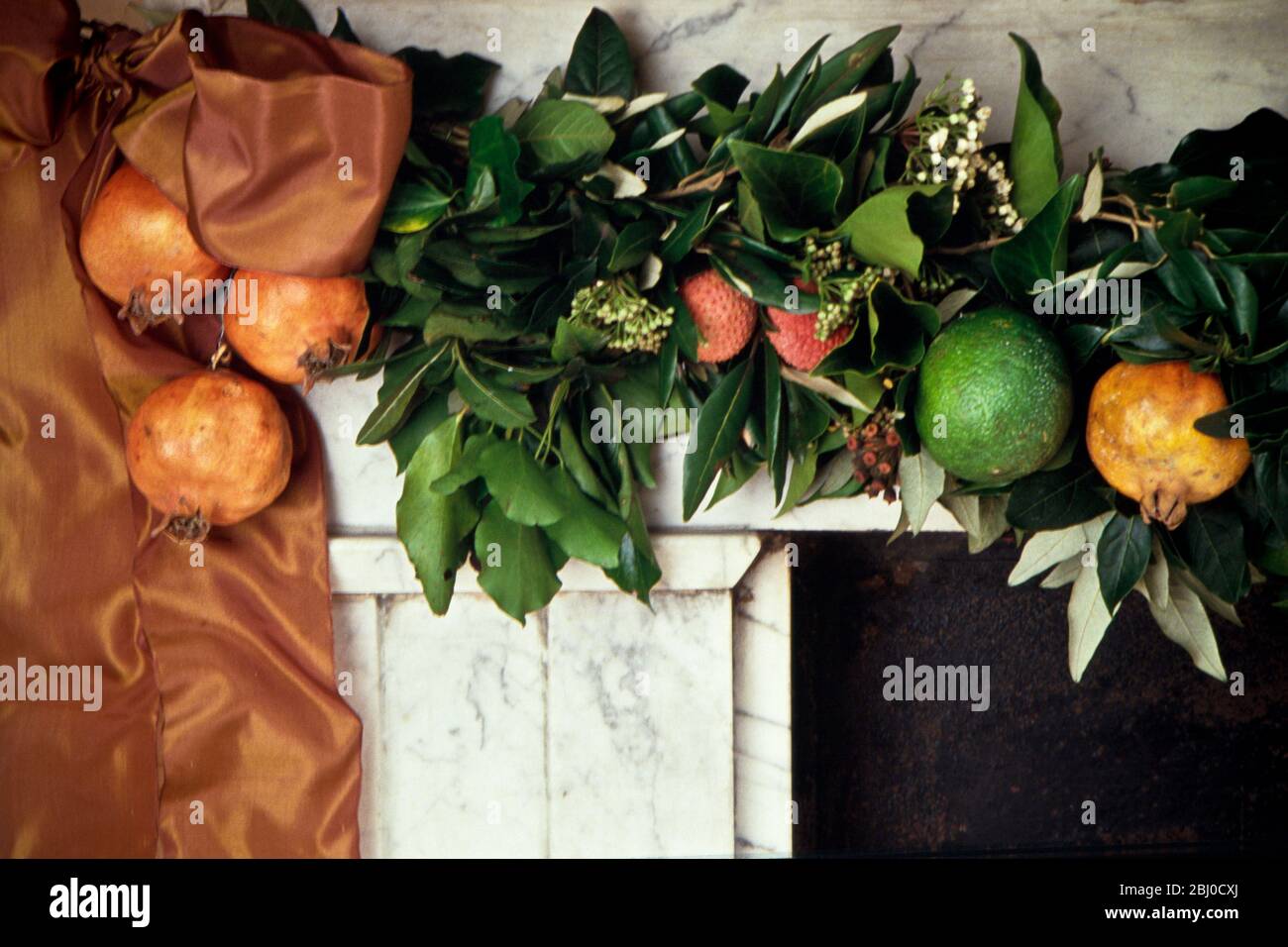 Opulento pezzo di camino con ricchi nastri e frutta fresca con verde naturale su antico mantelpiece in marmo. - Foto Stock