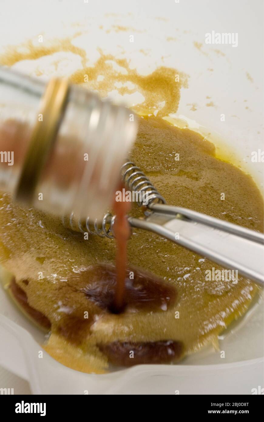 Preparazione di un classico condimento vinaigrette francese con senape, olio d'oliva e aceto di vino rosso, frittati insieme in una ciotola bianca - Foto Stock