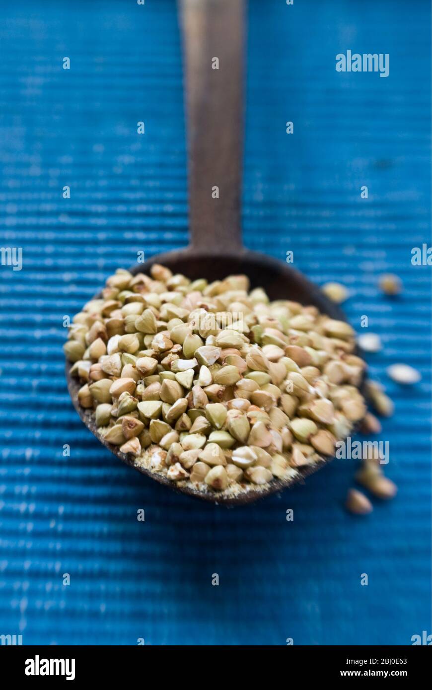 Cucchiaio di legno di grani di grano saraceno crudo interi su sfondo blu - Foto Stock