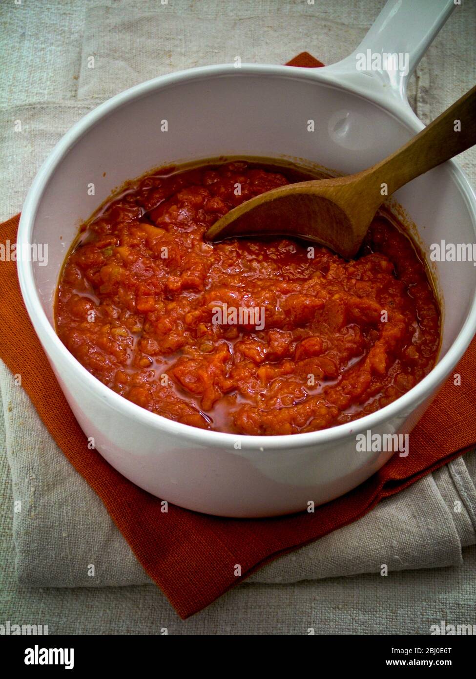 Preparare il salsa di tonato in una pentola bianca in ceramica, mescolando con un cucchiaio di legno - Foto Stock