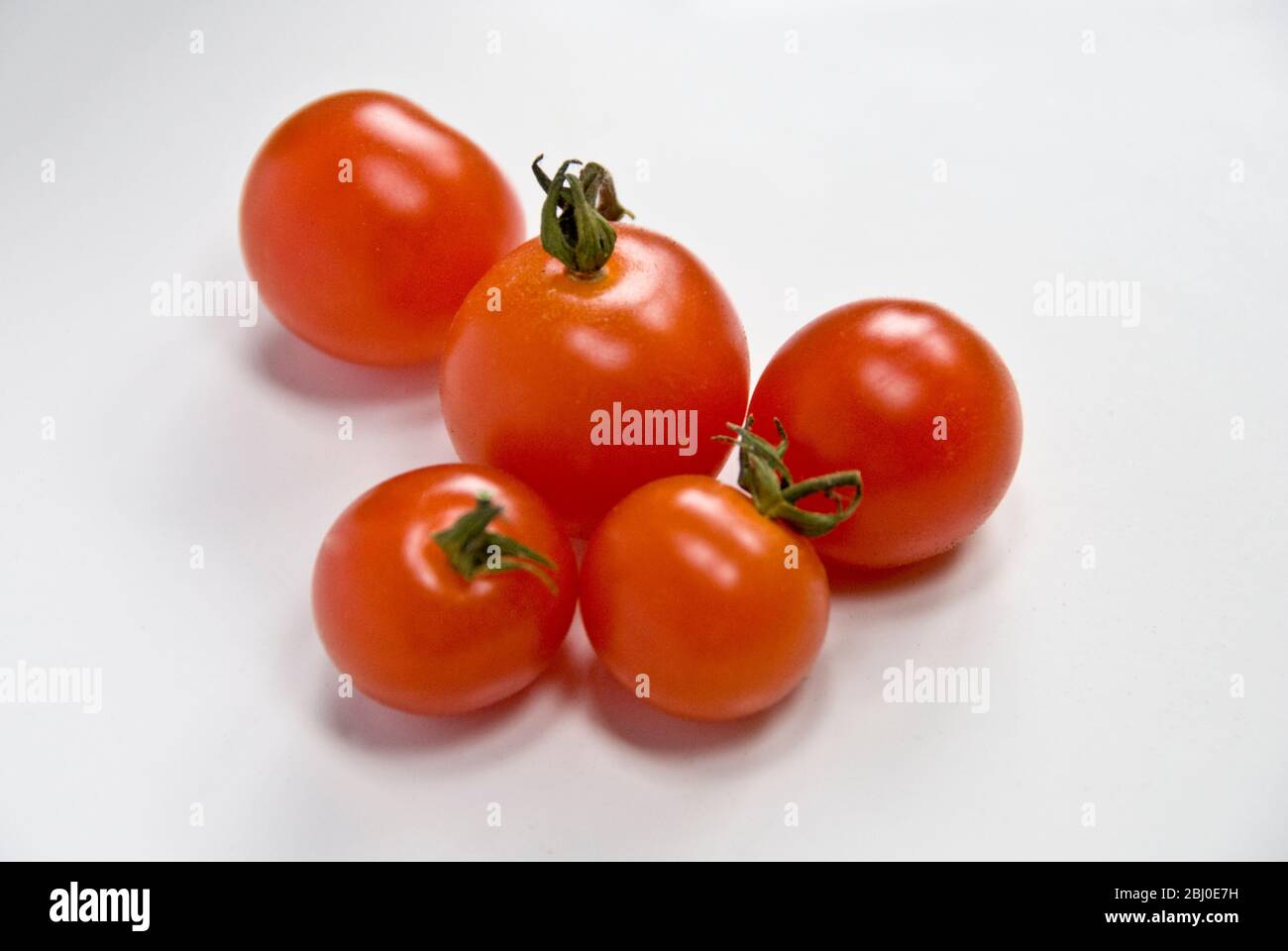 Cinque pomodori ciliegini rossi su superficie bianca - Foto Stock