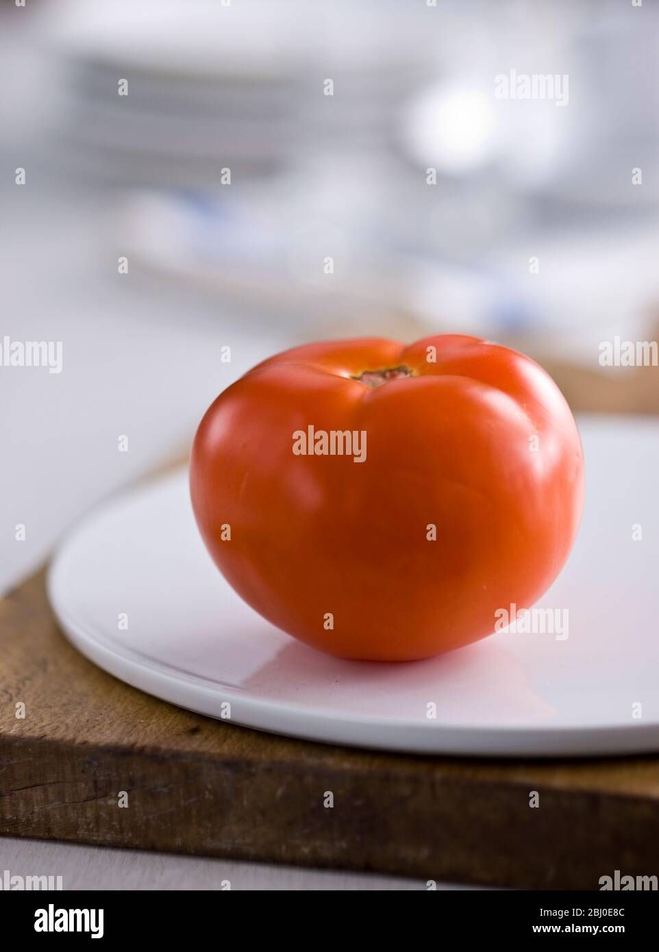Pomodoro rosso singolo su piatto bianco su tavola di legno - Foto Stock
