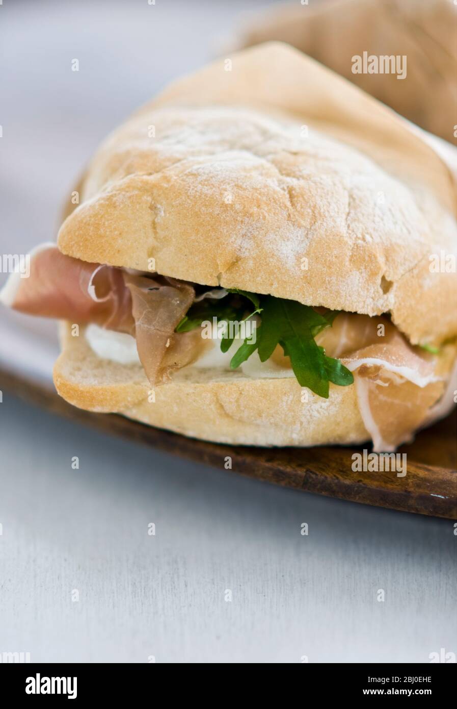 Sandwich di prosciutto italiano, di prosciutto di parma, mozzarella e rucola su pane leggero tipo ciabatta, avvolto in carta avvolta. - Foto Stock