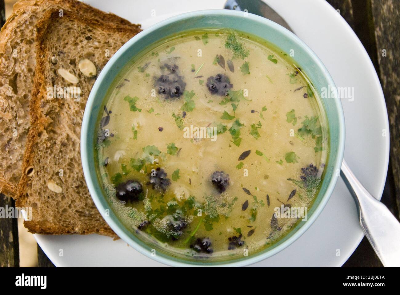 Ciotola di zuppa di pollo con trahana cipriota, broccoli germogliati viola e prezzemolo tritato, con pane integrale di segale seminato sul lato. - Foto Stock