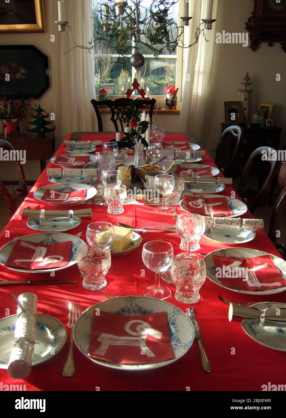 Luce del sole splendente all'interno con tavolo lungo posato per il pasto di Natale con tovaglia rossa e migliore cina, - Foto Stock