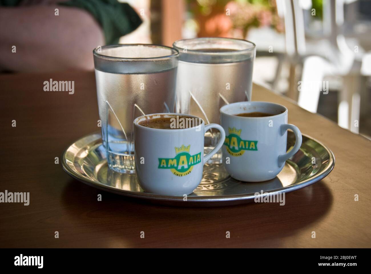 Due piccole tazze di caffè greco con bicchieri d'acqua di accompagnamento serviti in caffè cipriota sulle colline nel sud di Cipro - Foto Stock