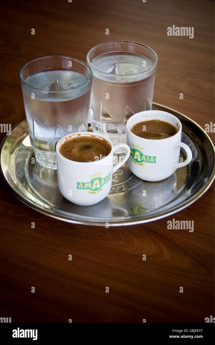 Due piccole tazze di caffè greco con bicchieri d'acqua di accompagnamento serviti in caffè cipriota sulle colline nel sud di Cipro - Foto Stock