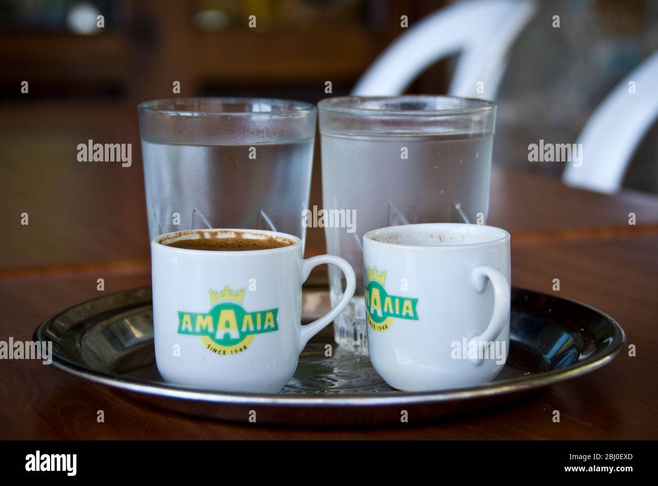 Due piccole tazze di caffè greco con bicchieri d'acqua di accompagnamento serviti in caffè cipriota sulle colline nel sud di Cipro - Foto Stock