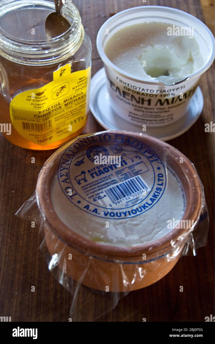 Scatola di plastica di Greek set latte di vacca yogurt e ceramica piatto di pecore latte yogurt, con miele cipriota, sul banco della cucina in casa cipriota - Foto Stock