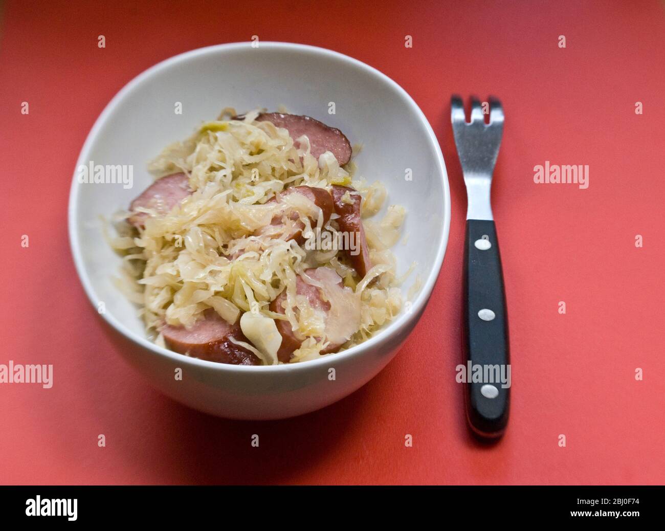 Piccolo piatto bianco di crauti tedeschi con pezzi di salsiccia affumicata - Foto Stock