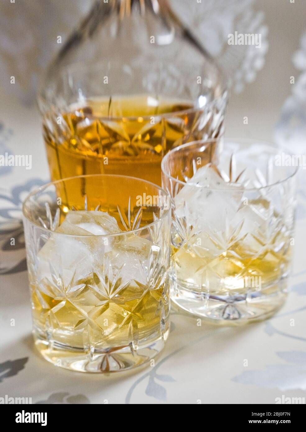 Scotch whisky su ghiaccio in vetro di cristallo di piombo tagliato su superficie decorativa argento, con decanter. - Foto Stock