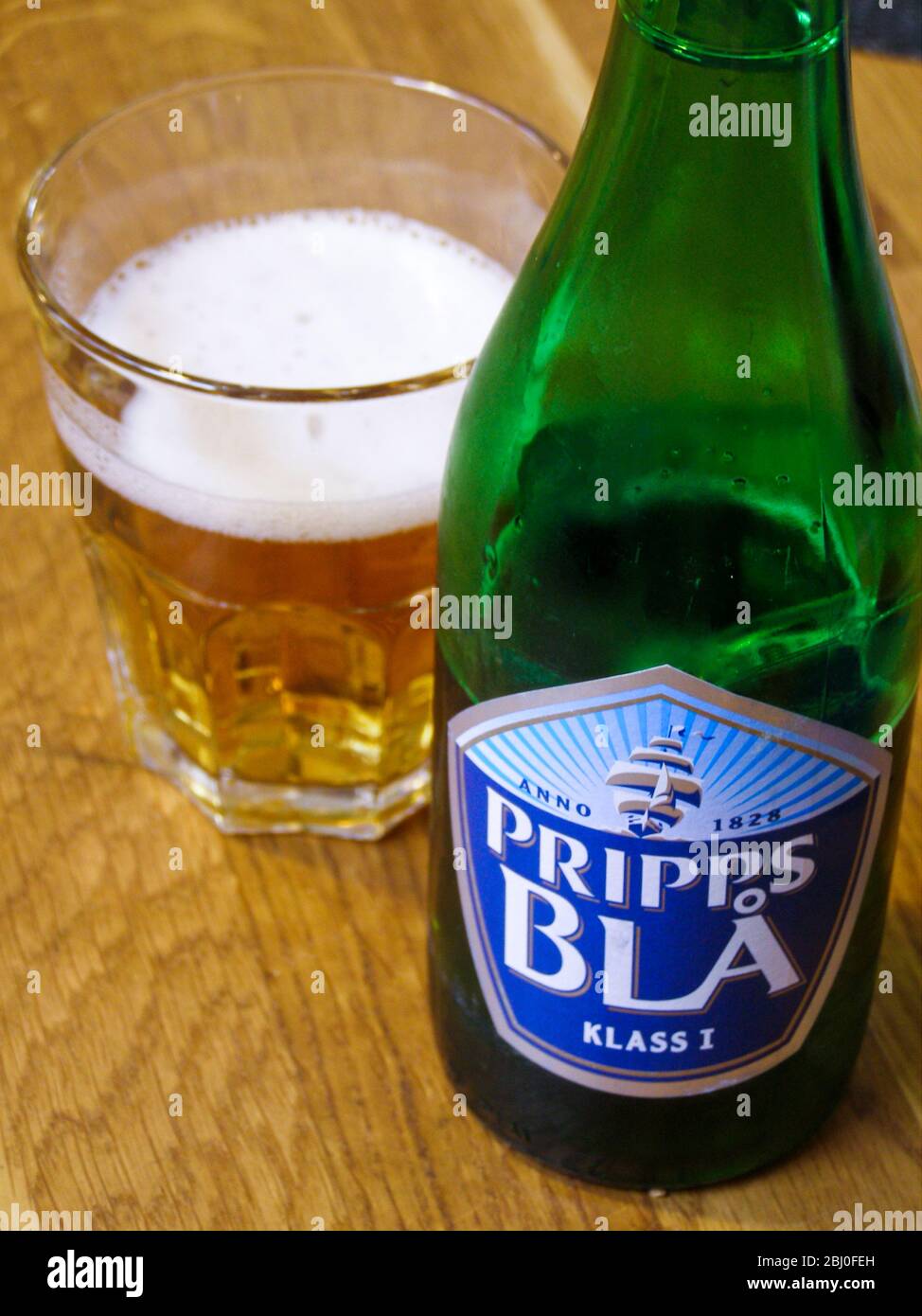 Prips BlÌ´ birra con alcuni versate in un bicchiere su tavolo da ristorante in legno. Si tratta di una birra molto leggera, comunemente bevuta a pranzo o quando il designa Foto Stock