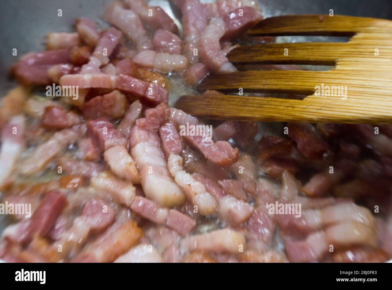 Cottura di pezzi tritati di pancetta striata in una padella. Conosciuta come pancetta in Italia e lardi in Francia - Foto Stock