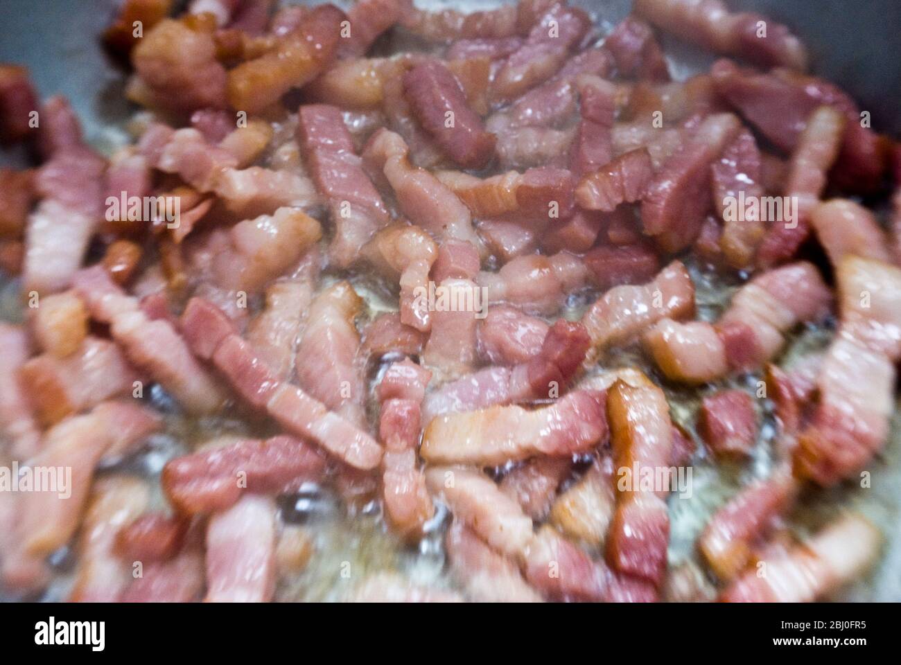 Cottura di pezzi tritati di pancetta striata in una padella. Conosciuta come pancetta in Italia e lardi in Francia - Foto Stock