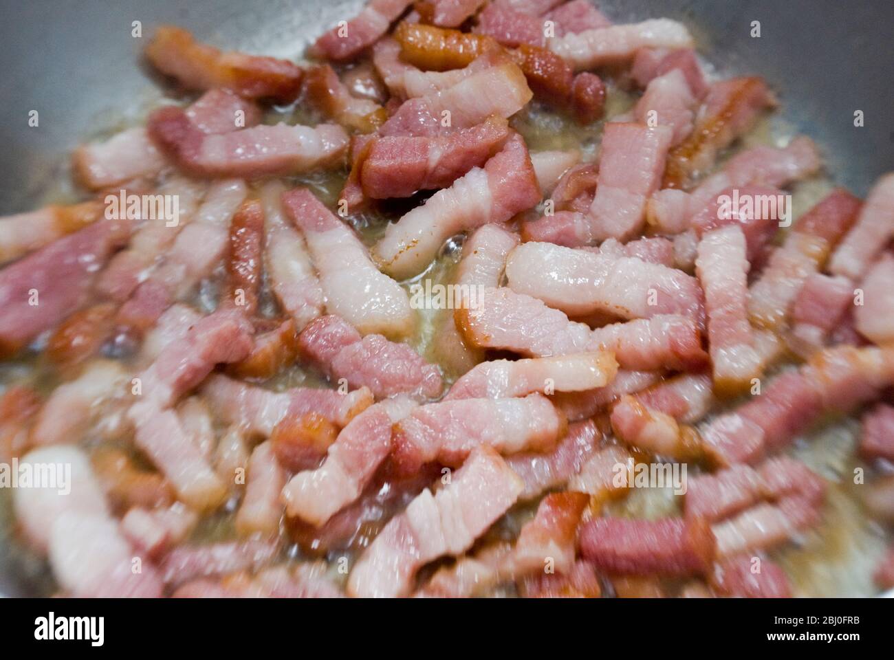 Cottura di pezzi tritati di pancetta striata in una padella. Conosciuta come pancetta in Italia e lardi in Francia - Foto Stock
