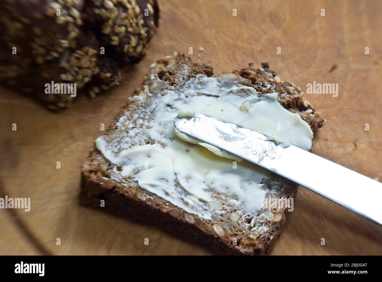 Spalmare il burro su una fetta di pane di segale in stile scandinavo. - Foto Stock