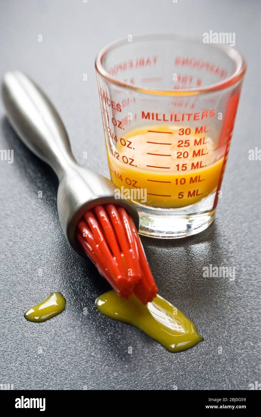 Tuorlo d'uovo in piccolo bicchiere graduato con moderno pennello da pasticceria con 'setole' in silicone rosso - Foto Stock
