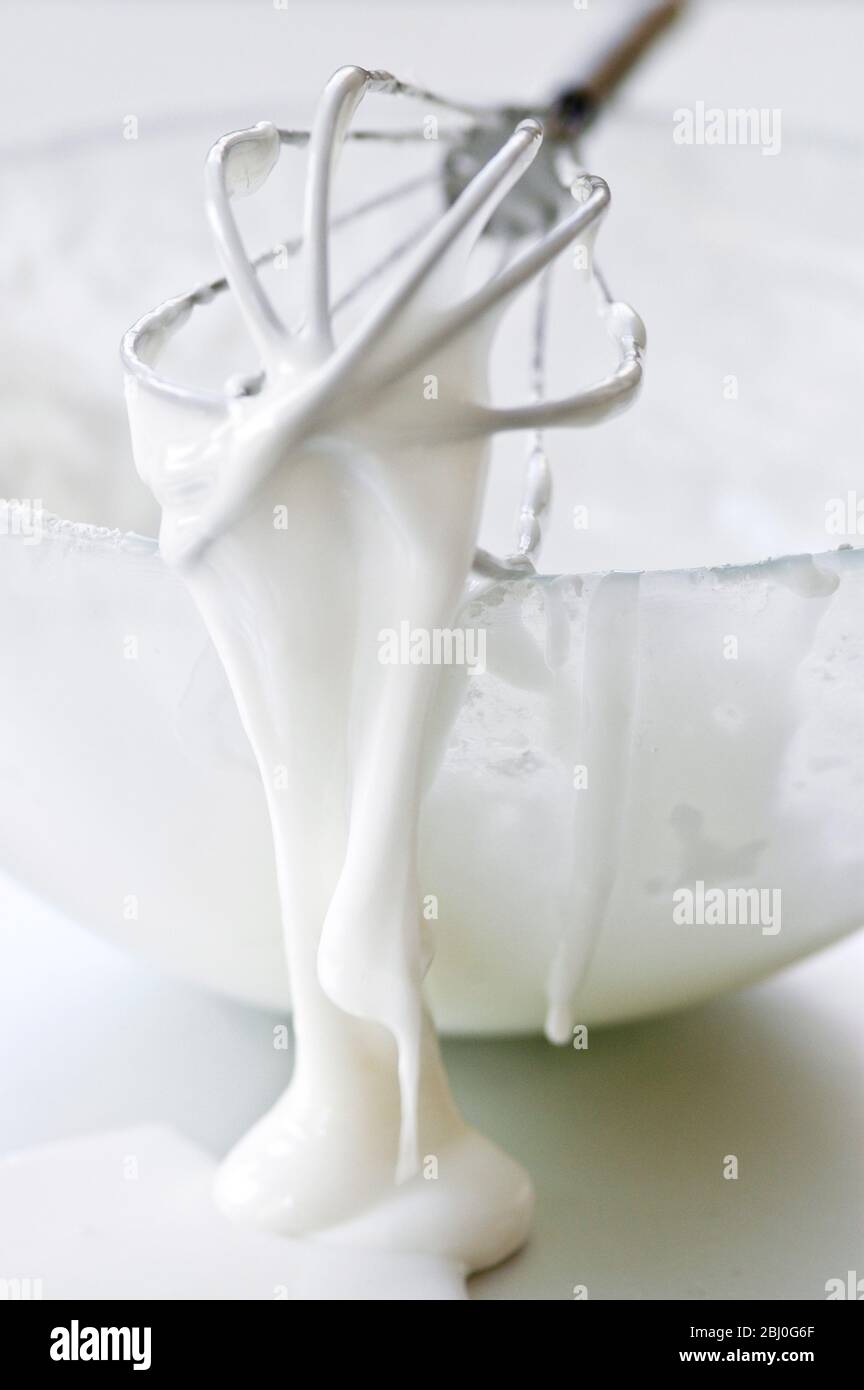 Ciotola di glassa bianca con frusta di palloncino gocciolante - Foto Stock