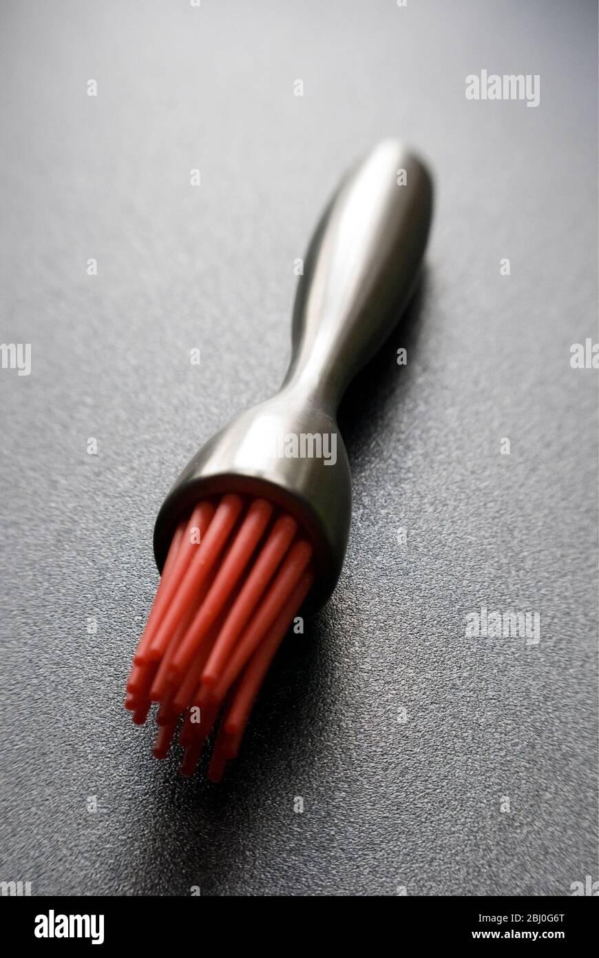 Spazzola per pasticceria moderna con setole in silicone rosso su superficie ruvida scura - Foto Stock