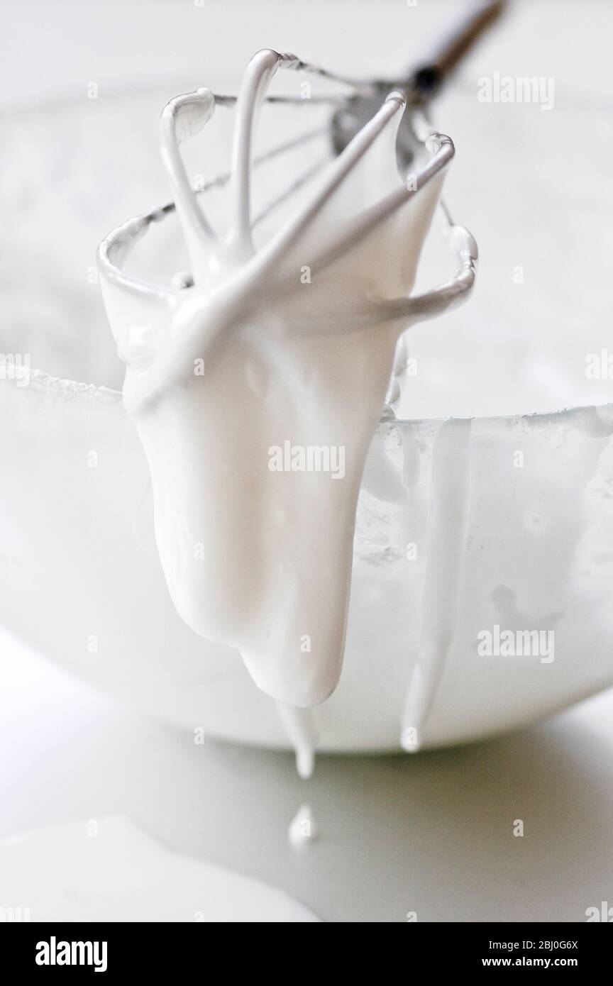 Ciotola di glassa bianca con frusta di palloncino gocciolante - Foto Stock