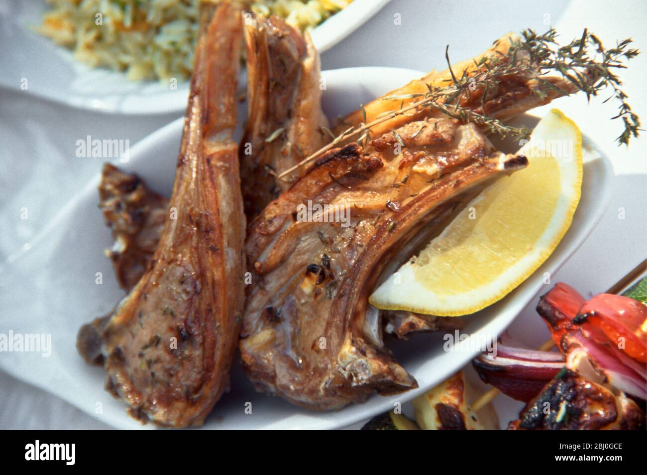 Costolette di agnello grigliate al barbecue con timo fresco, servite con spicchio di limone. - Foto Stock