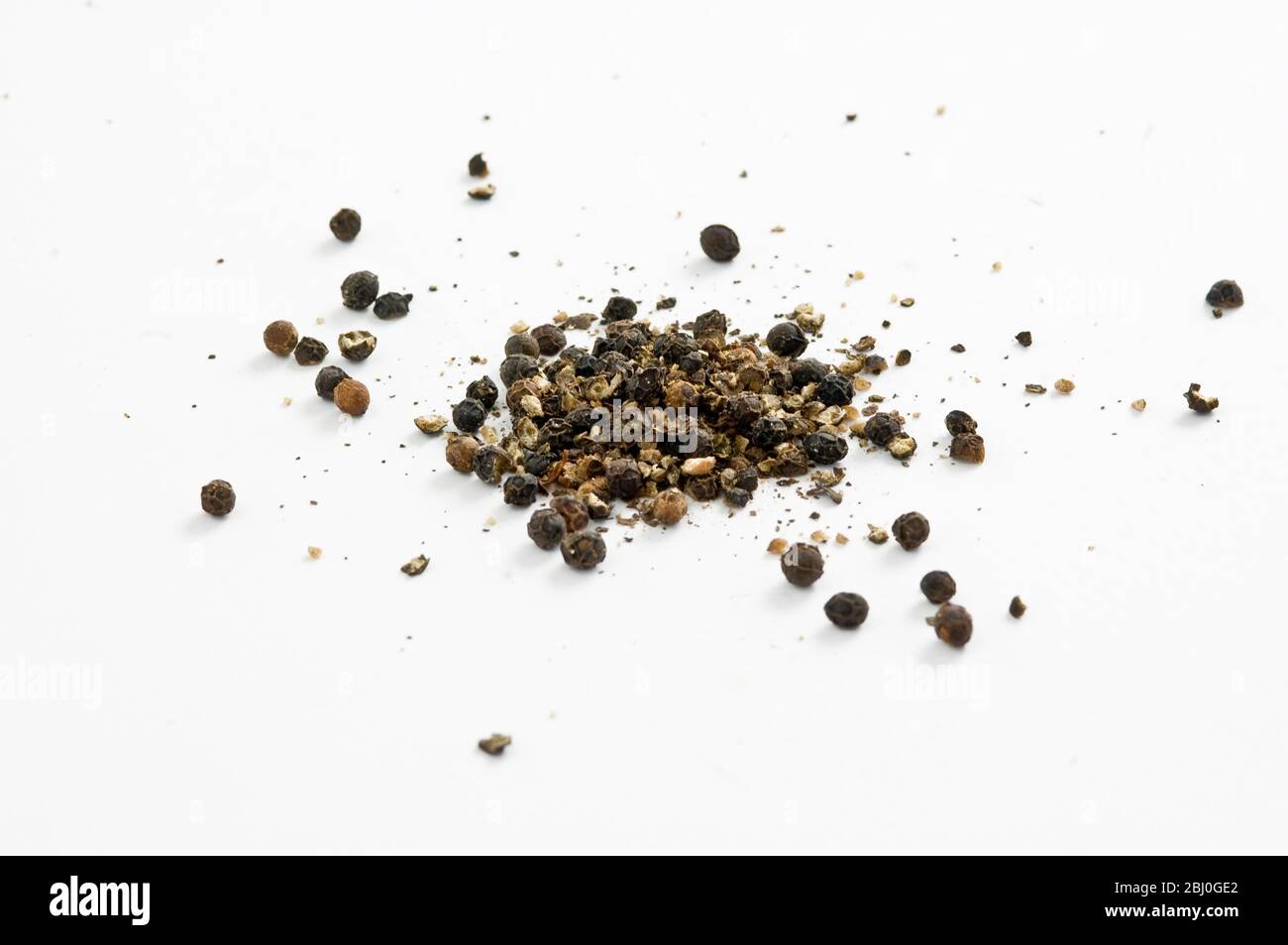 Peppercorn neri leggermente schiacciati su superficie bianca - Foto Stock