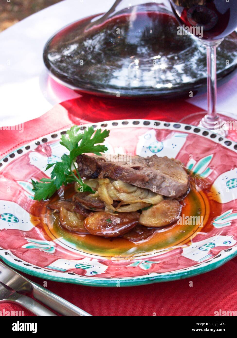 Lombata di maiale avvolta in pancetta con cipolle e patate servite a mano dipinte piatti italiani all'aperto - Foto Stock