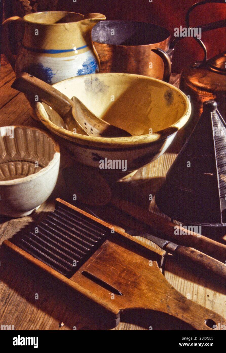 Una collezione di vecchi e antichi kitchenalia, attrezzi e attrezzature tra cui caraffe, ciotole, muffe, setaccio, padelle e bollitore in cina, metallo e rame. - Foto Stock