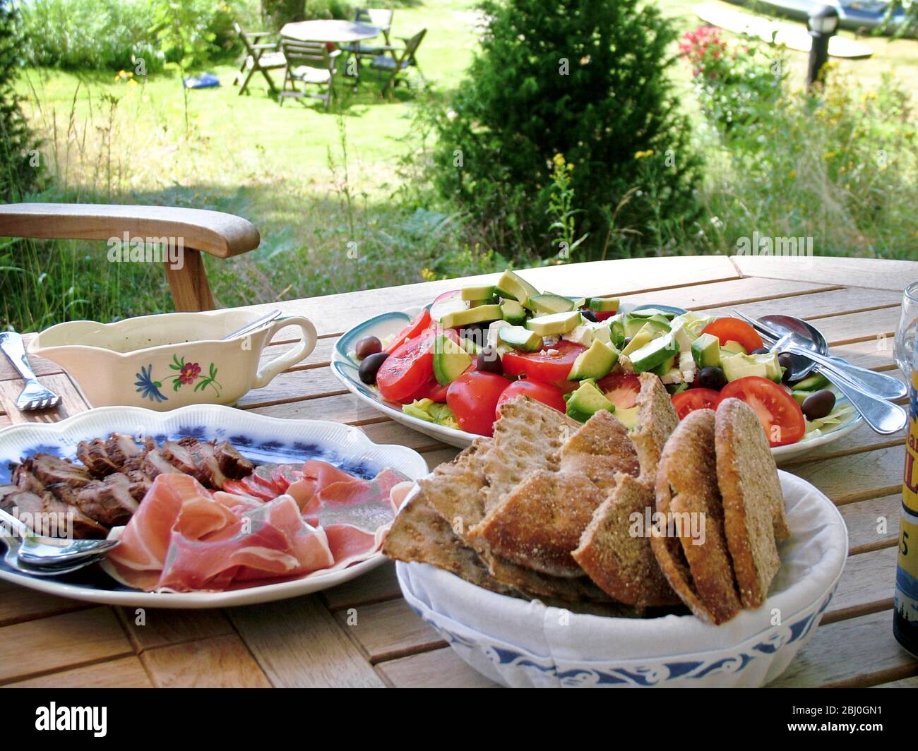 Pranzo estivo svedese di prosciutto, salsiccia e carne fredda e insalata con pane di segale piatto, servito su tavolo di legno all'ombra degli alberi - Foto Stock